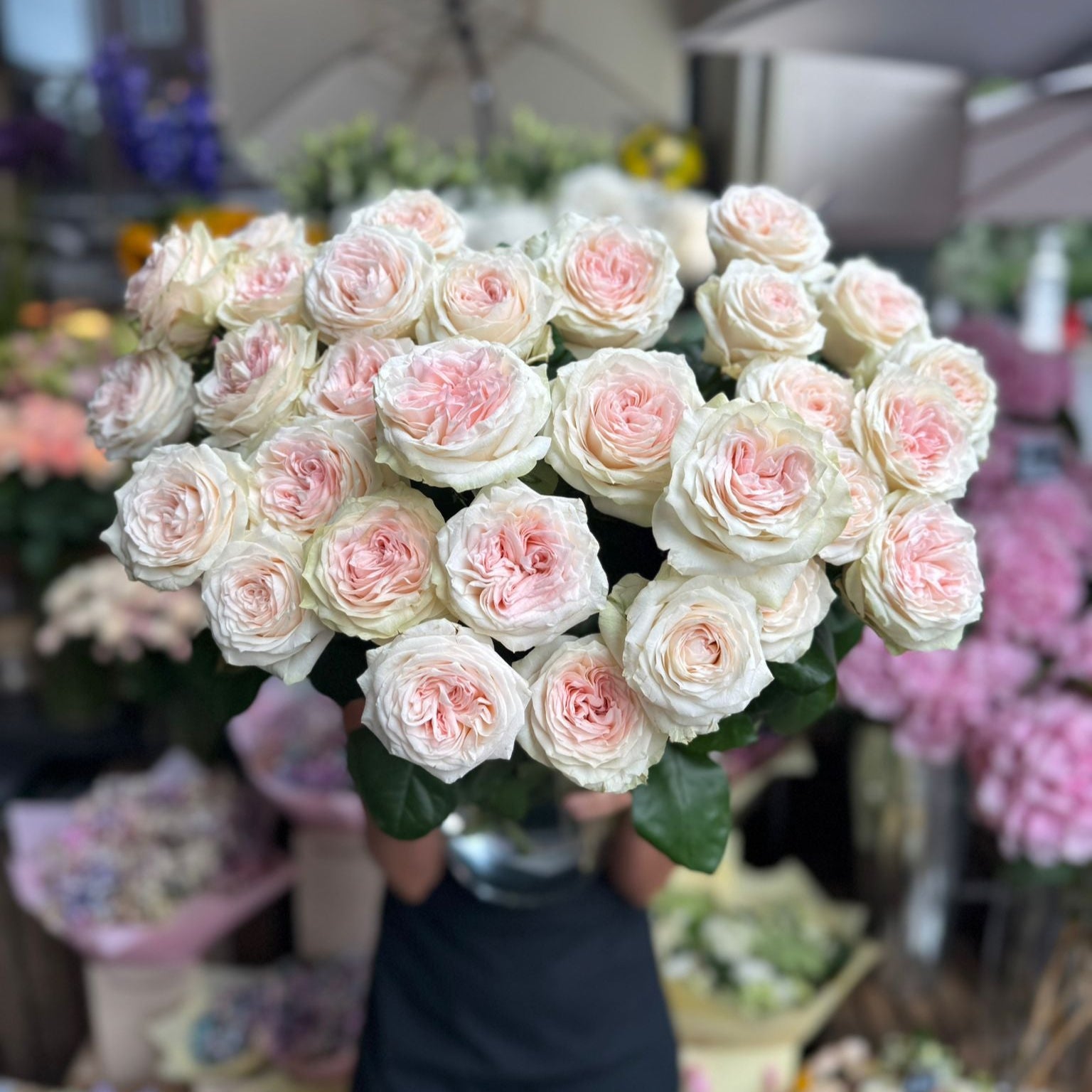 Bouquet of pink and white flowers held by a person with blurred floral background