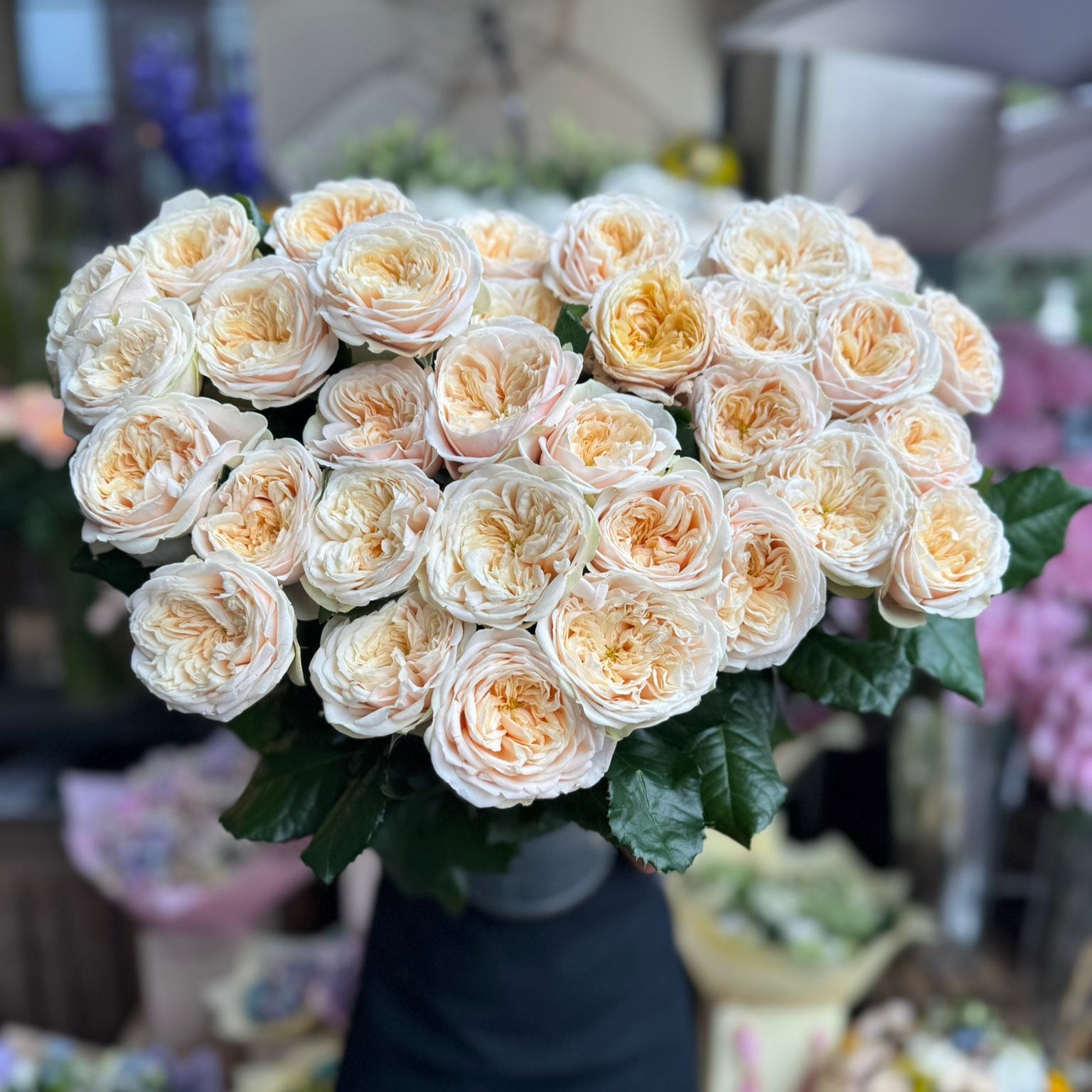 Bouquet of white and beige roses on a black vase with blurred floral background