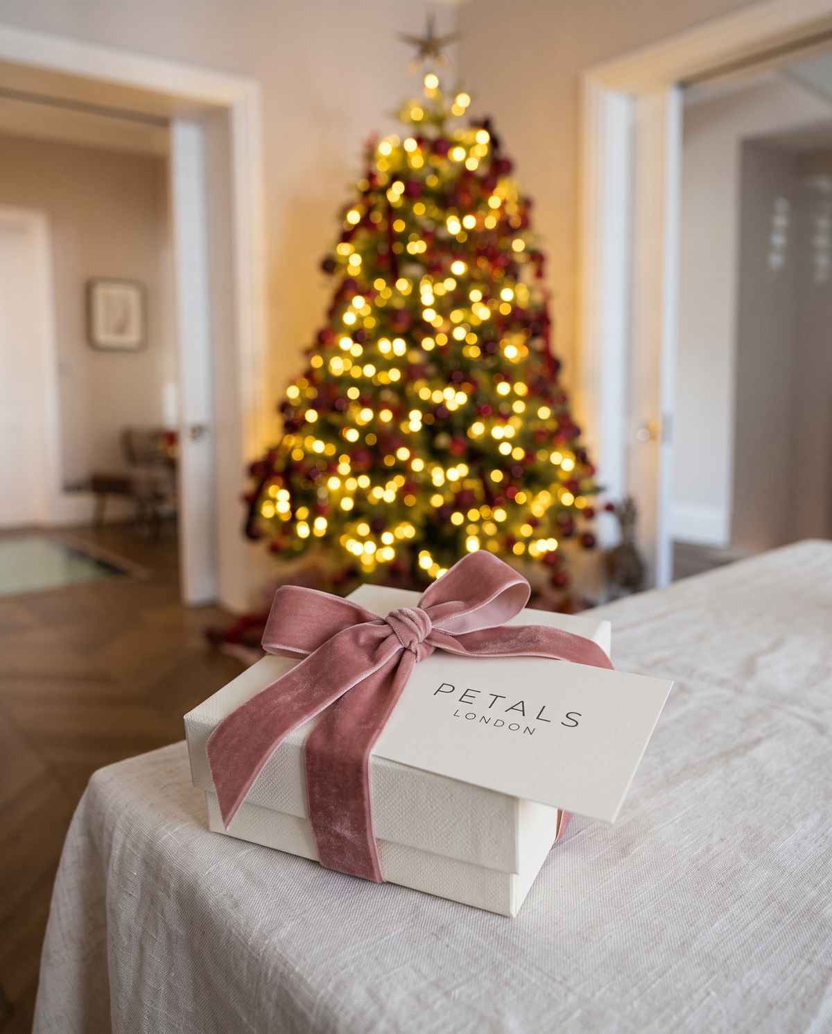 Petals London gift box with a pink velvet ribbon in front of a lit Christmas tree