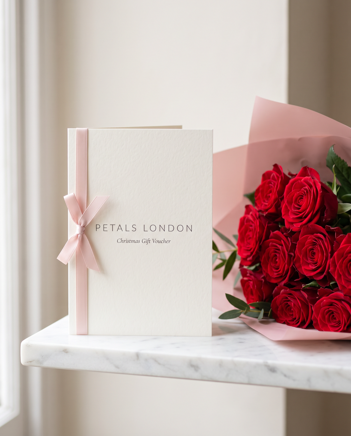 Petals London Christmas Gift Voucher card beside a bouquet of red roses