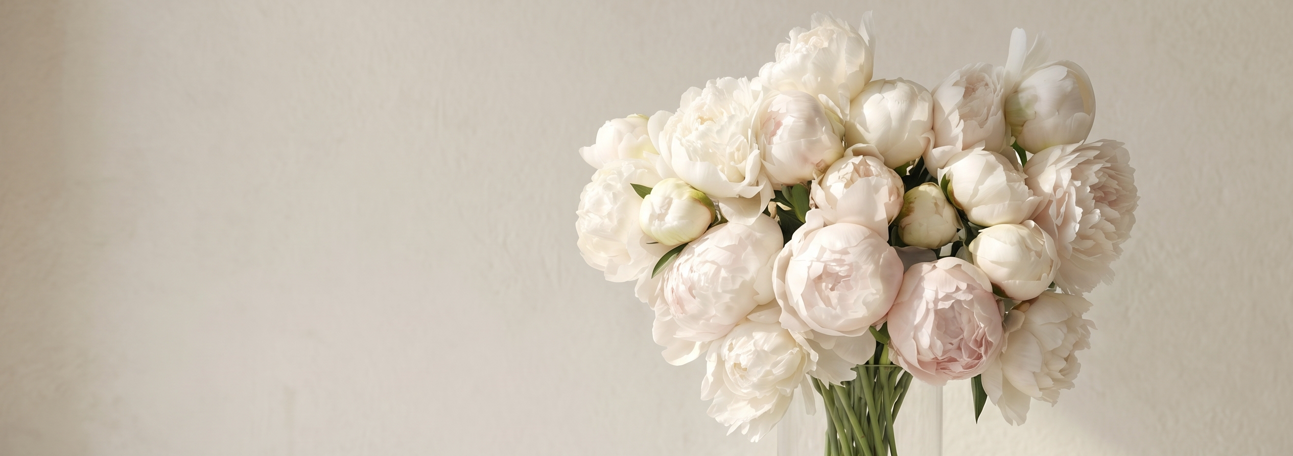 Bouquet of white and pink flowers in a clear vase on a white surface with a light gray background