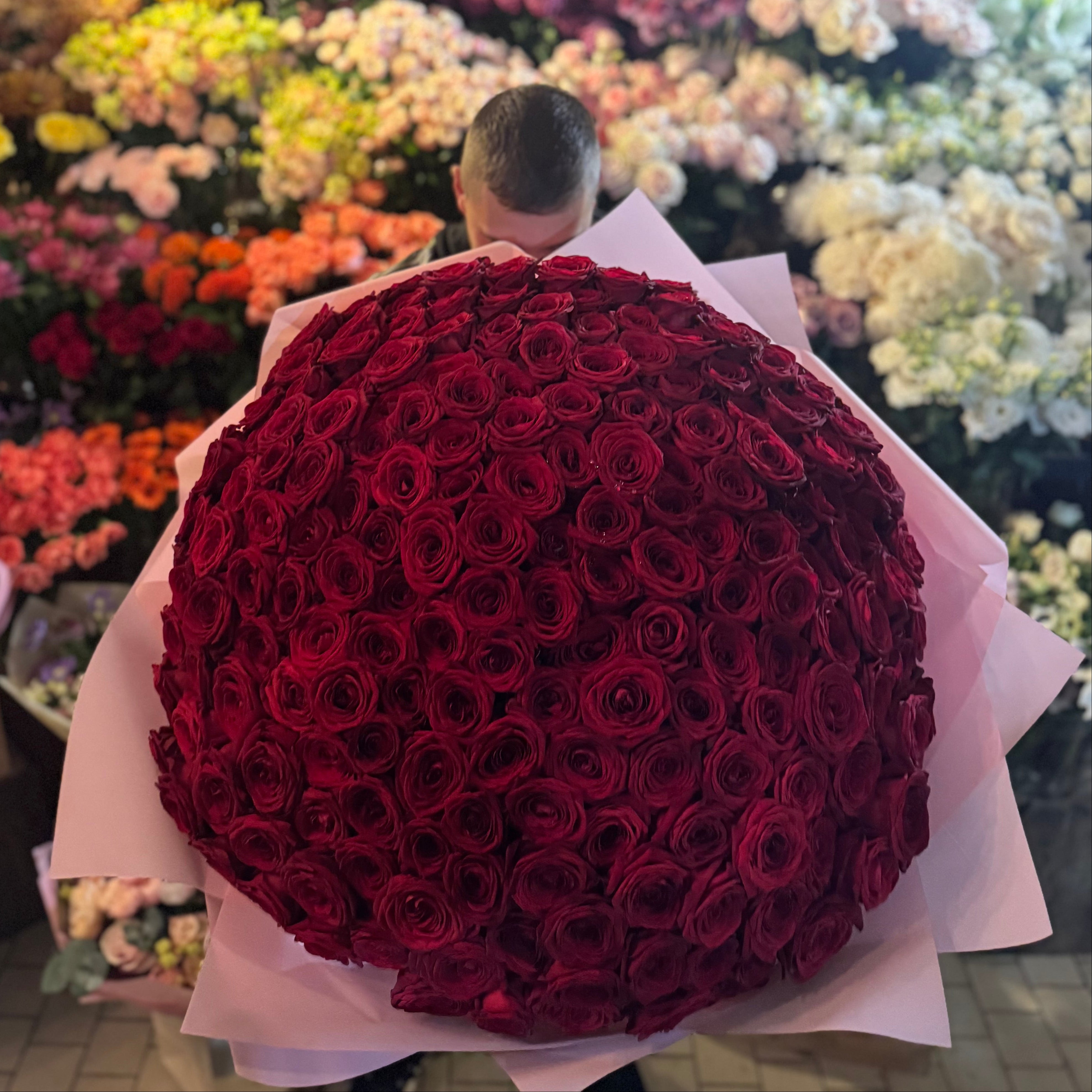 Person holding a large bouquet of red roses in a flower shop.