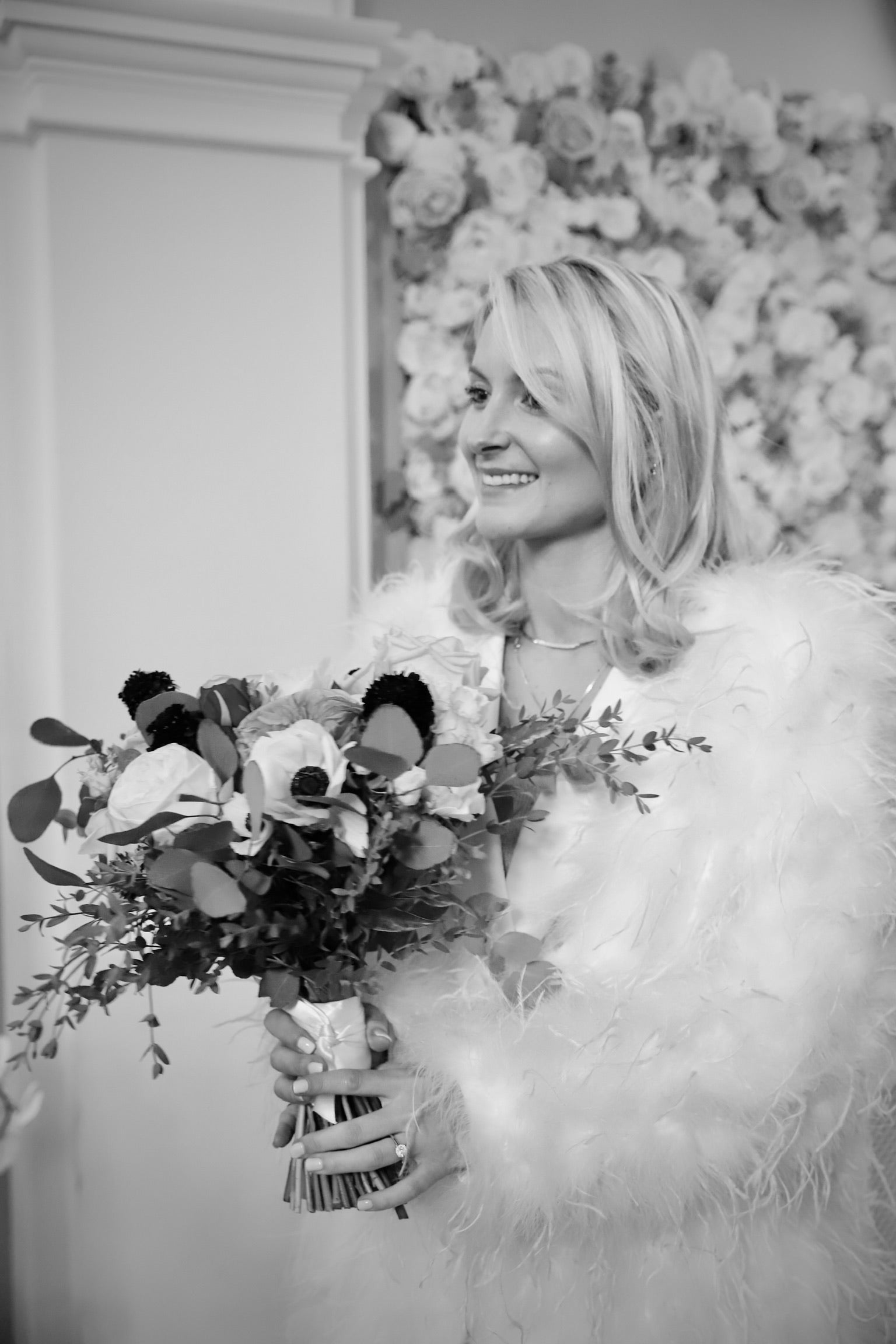 Bride smiling with bouquet in front of floral wall backdrop