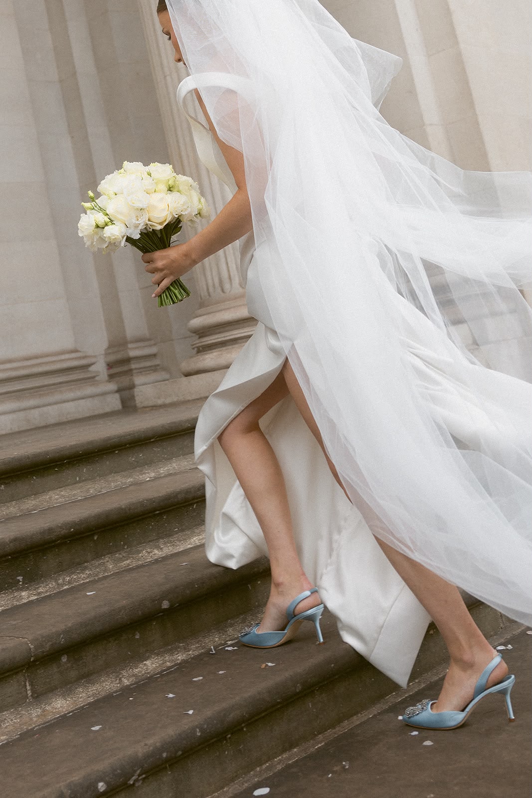 Bride ascending steps with flowing veil and white bouquet